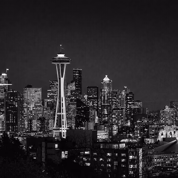 Black and white Seattle skyline at night with the Space Needle illuminated above downtown buildings.