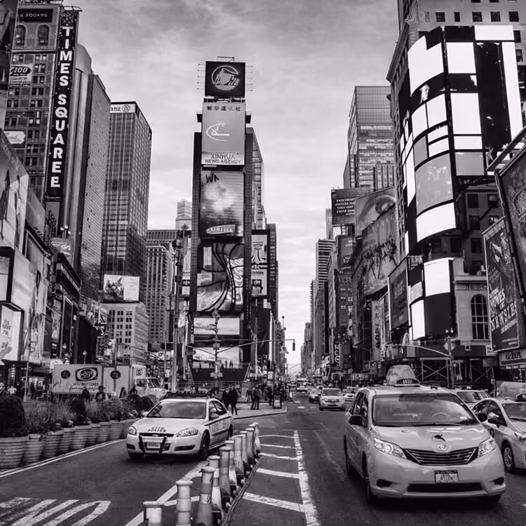 Black and white view of Times Square in New York City with illuminated billboards, taxis, and busy traffic.