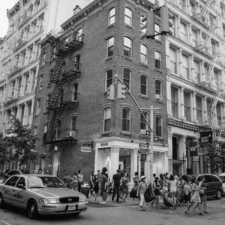 Historic SoHo corner building in New York City with cast-iron architecture and pedestrians crossing the street.