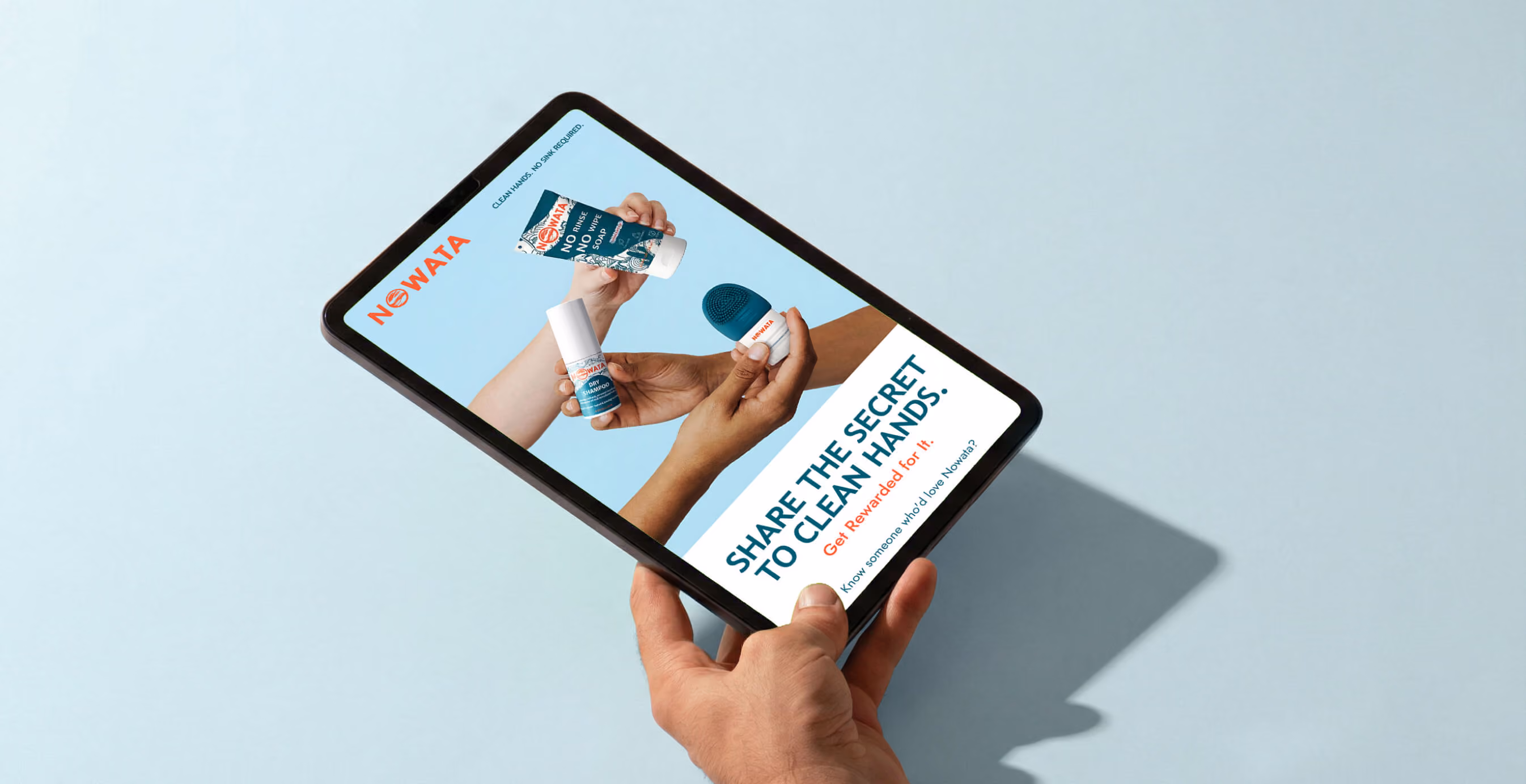 Close-up of hands holding a tablet featuring NOWATA products and referral messaging encouraging users to share and get rewarded.