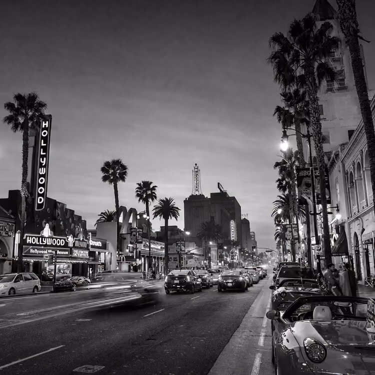 Hollywood Boulevard at night with palm trees, neon theater signs, and busy street traffic in Los Angeles.