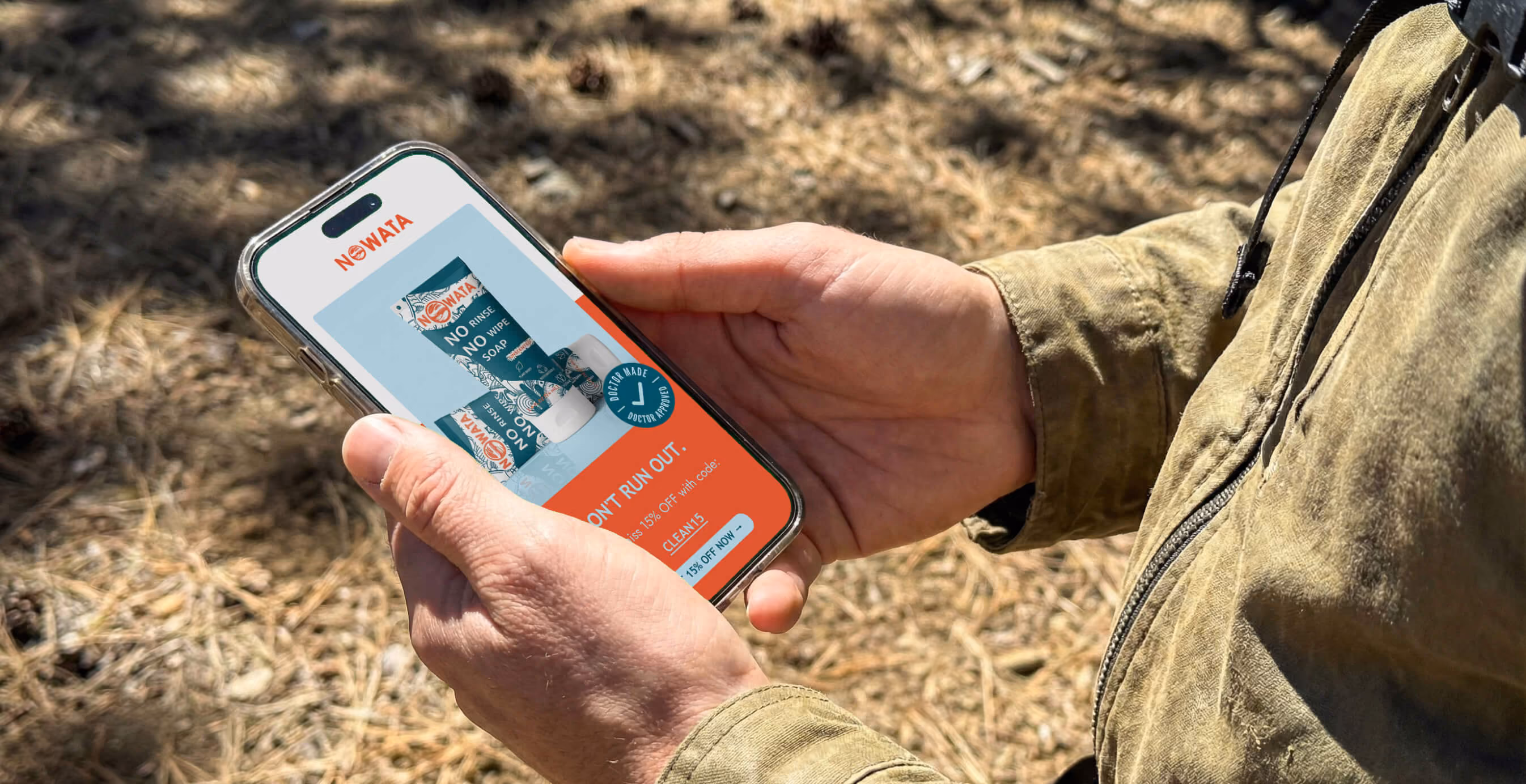 Person holding a smartphone outdoors displaying a NOWATA ad for rinse-free, no-wipe soap with a promotional discount offer.
