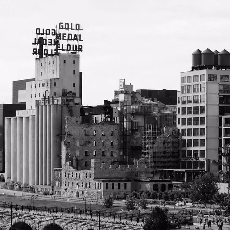 Black and white photo of the historic Gold Medal Flour mill building and silos along the Mississippi River in downtown Minneapolis.