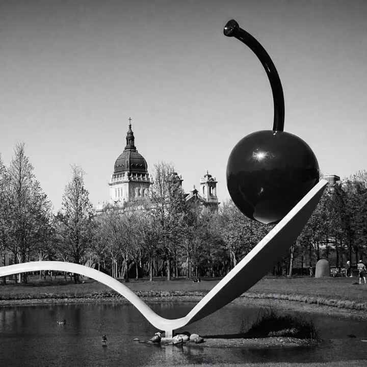 Black and white image of the Spoonbridge and Cherry sculpture in the Minneapolis Sculpture Garden with the Basilica of Saint Mary in the background.