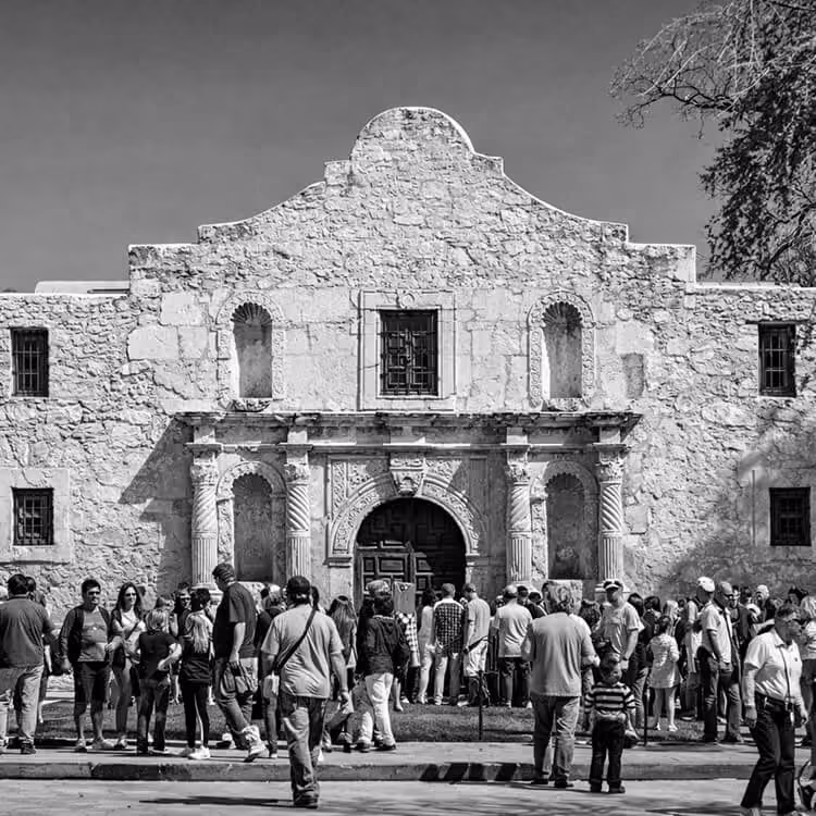 Black and white photo of visitors gathered in front of the historic Alamo Mission in downtown San Antonio, Texas.