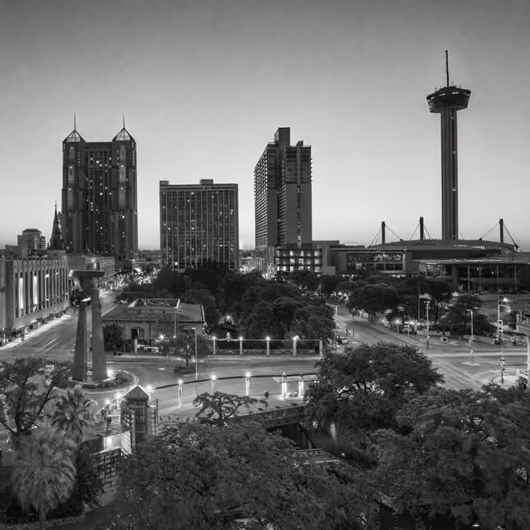 Black and white cityscape of downtown San Antonio featuring the Tower of the Americas and surrounding skyline at dusk.