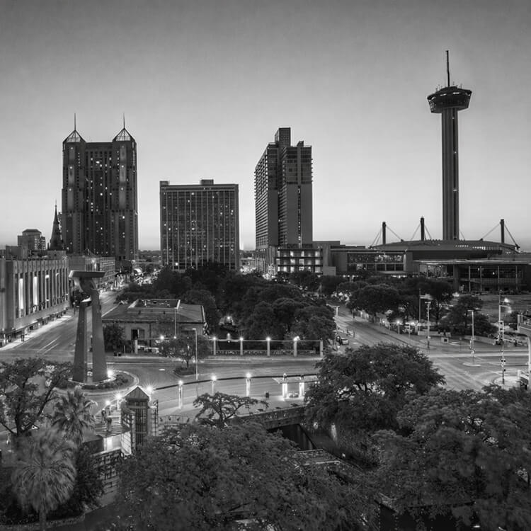 Black and white cityscape of downtown San Antonio featuring the Tower of the Americas and surrounding skyline at dusk.