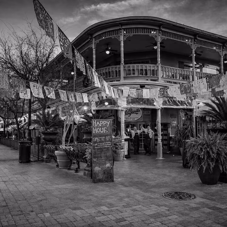 Black and white street view of a historic restaurant with balcony and festive decorations along the San Antonio River Walk.