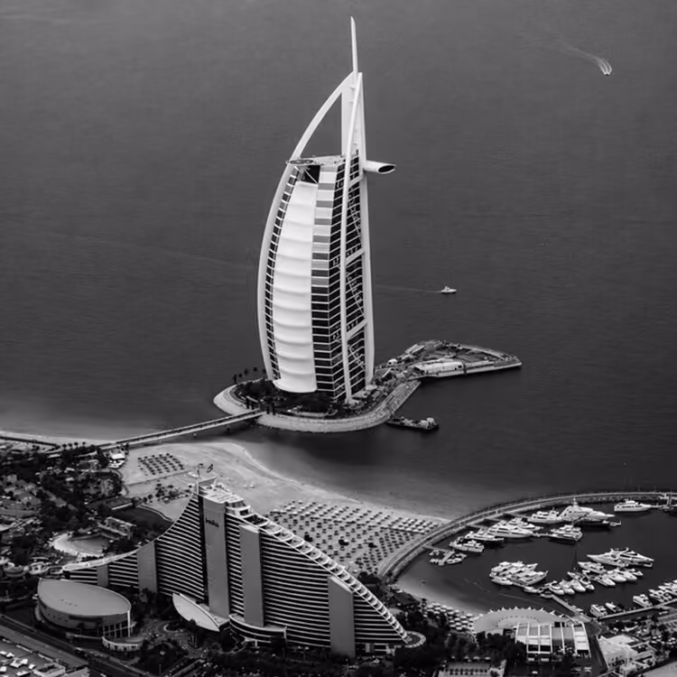 Black and white aerial view of the Burj Al Arab hotel on its island with surrounding coastline and luxury resorts in Dubai.