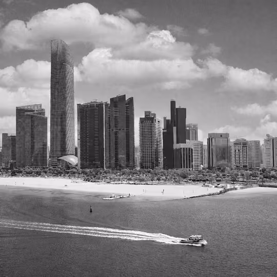 Black and white image of Dubai’s beachfront skyline with modern towers and a boat moving across the water.