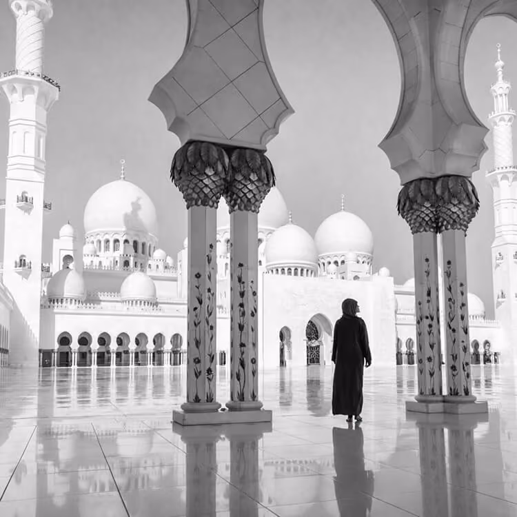 Black and white view of a person walking through the grand arches of Sheikh Zayed Grand Mosque in Abu Dhabi.