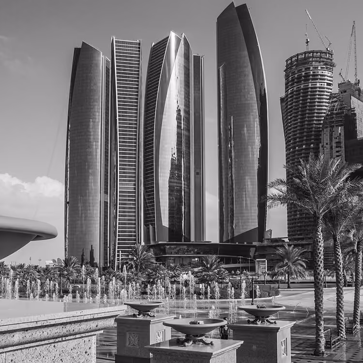 Black and white image of Etihad Towers rising above landscaped fountains and palm trees in downtown Abu Dhabi.