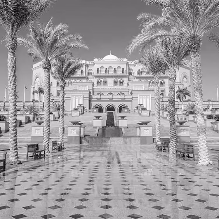 Black and white front view of Emirates Palace hotel framed by palm trees and a patterned courtyard in Abu Dhabi.