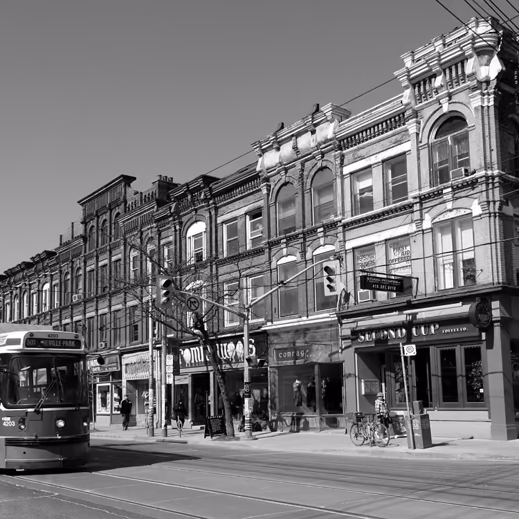 Black and white street scene of Queen Street West with a streetcar, storefronts, and historic buildings in Toronto.