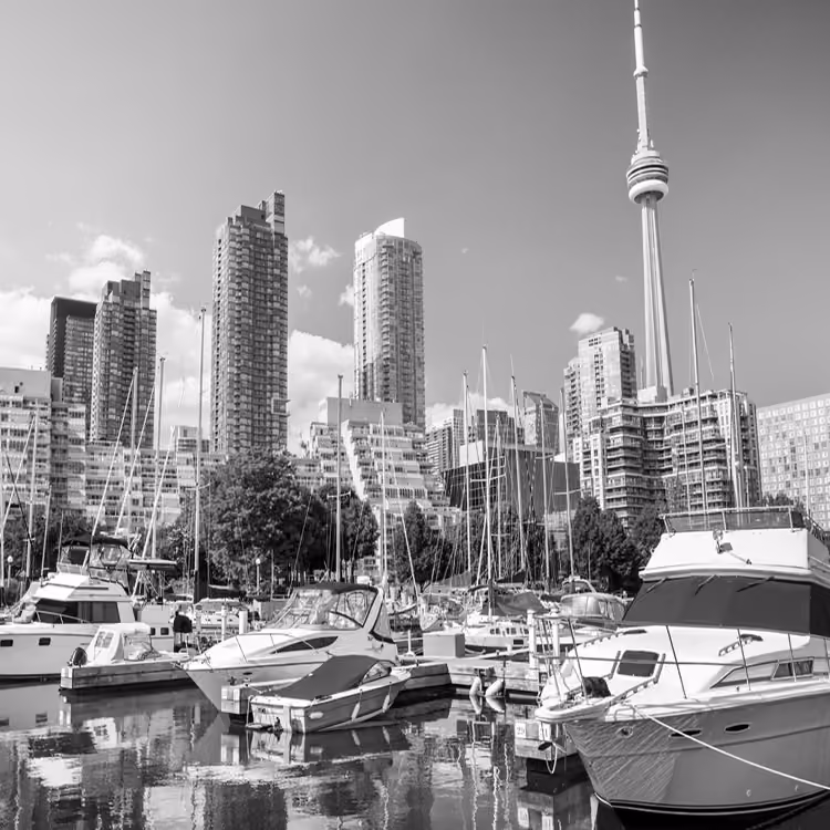 Black and white view of Toronto’s waterfront with boats docked in the marina and the CN Tower rising above the skyline.