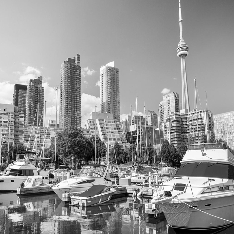 Black and white view of Toronto’s waterfront with boats docked in the marina and the CN Tower rising above the skyline.