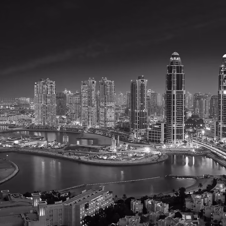 Black and white aerial view of Doha skyline at night with illuminated skyscrapers and waterfront reflections in Qatar.