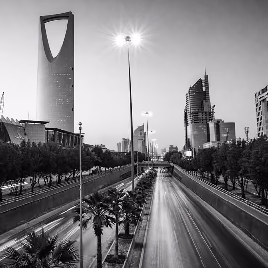 Black and white view of Riyadh skyline featuring the Kingdom Centre Tower above a busy highway at dusk.