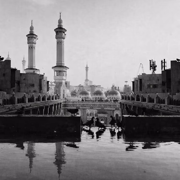 Black and white view of a mosque with tall minarets and reflective courtyard in a Saudi Arabian city.