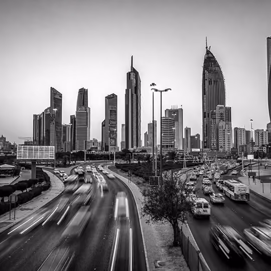 Black and white image of a busy highway with motion blur leading into Kuwait City’s modern skyline.
