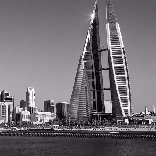 Black and white image of the Bahrain World Trade Center twin towers with integrated wind turbines overlooking the waterfront.