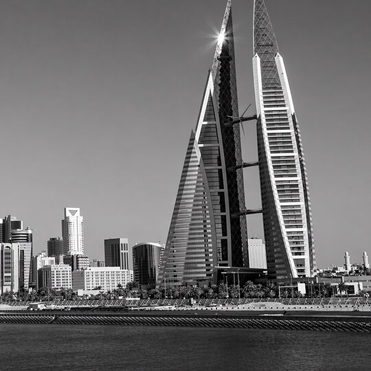 Black and white image of the Bahrain World Trade Center twin towers with integrated wind turbines overlooking the waterfront.