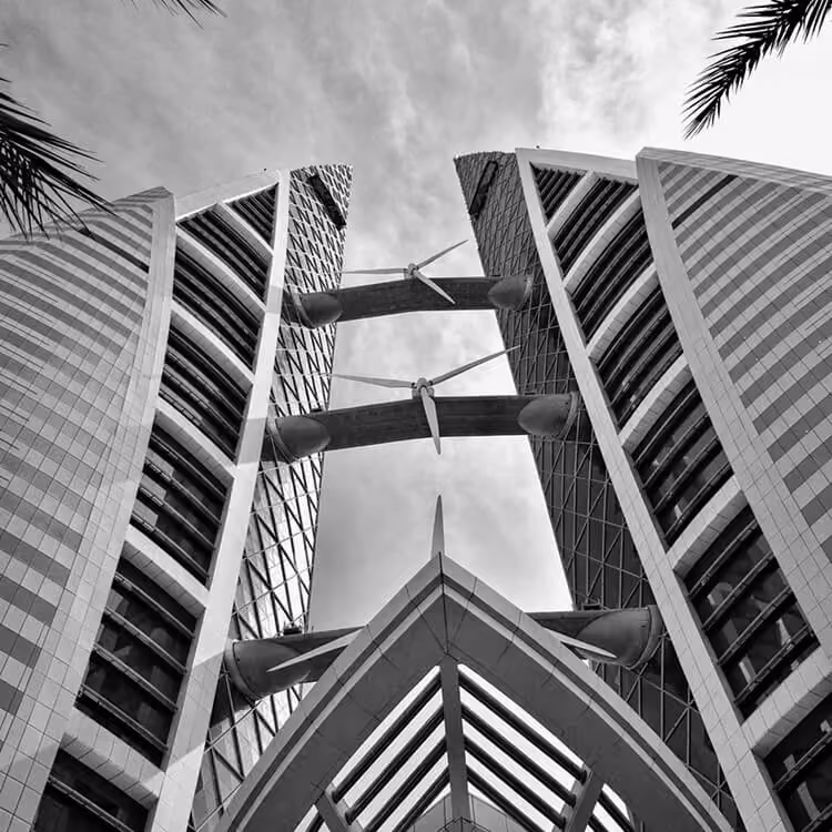 Black and white upward view of Bahrain World Trade Center highlighting its twin towers and wind turbines.