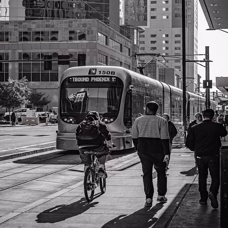 Black and white image of Phoenix light rail train with pedestrians and cyclist in an urban downtown setting.