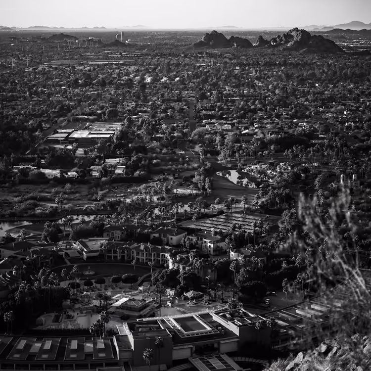 Black and white aerial view of Phoenix neighborhoods with desert mountains in the background.