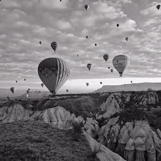 Black and white image of hot air balloons flying over Cappadocia rock formations in Turkey.