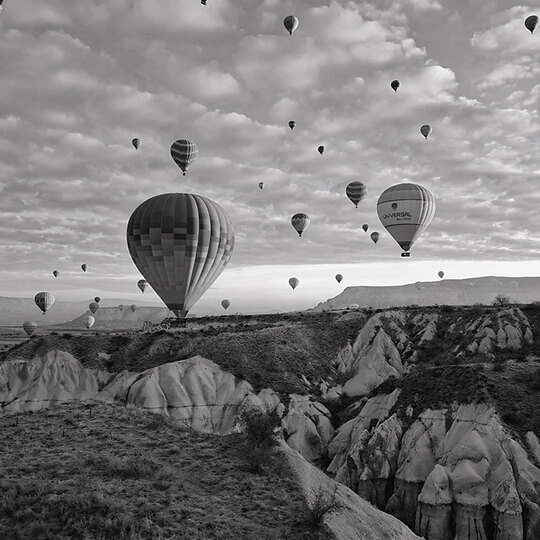 Black and white image of hot air balloons flying over Cappadocia rock formations in Turkey.