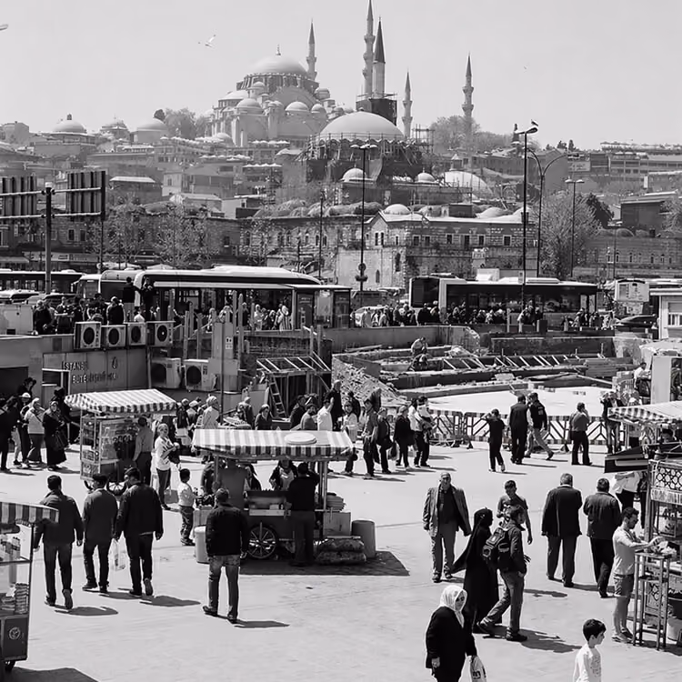 Black and white image of a busy public square in Istanbul with people, vendors, and mosques.