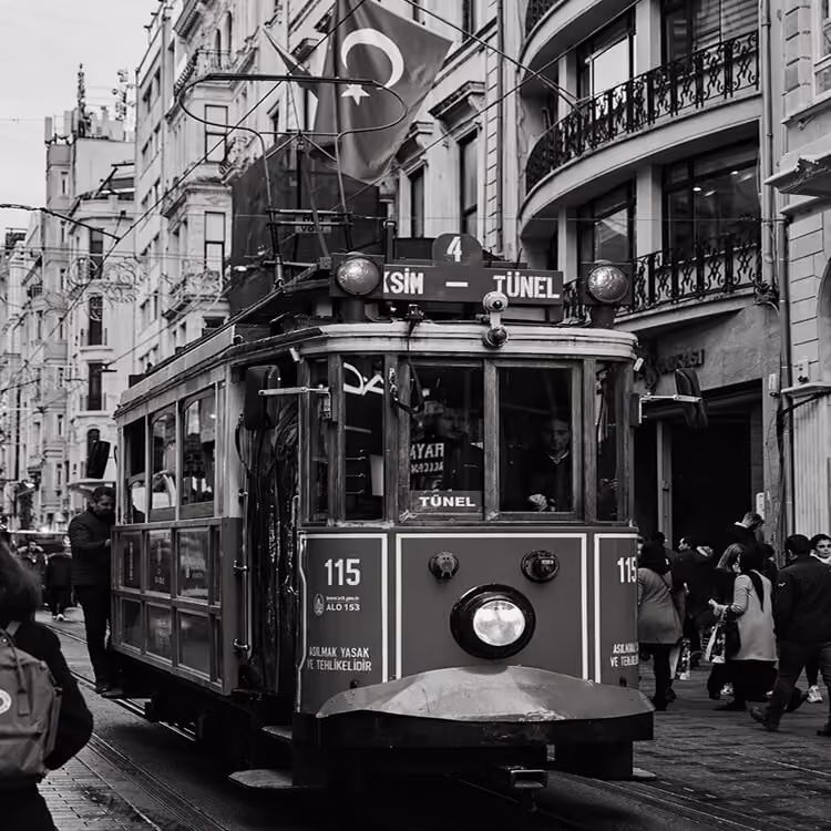 Black and white image of a vintage red tram on Istiklal Street with pedestrians and Turkish flags.