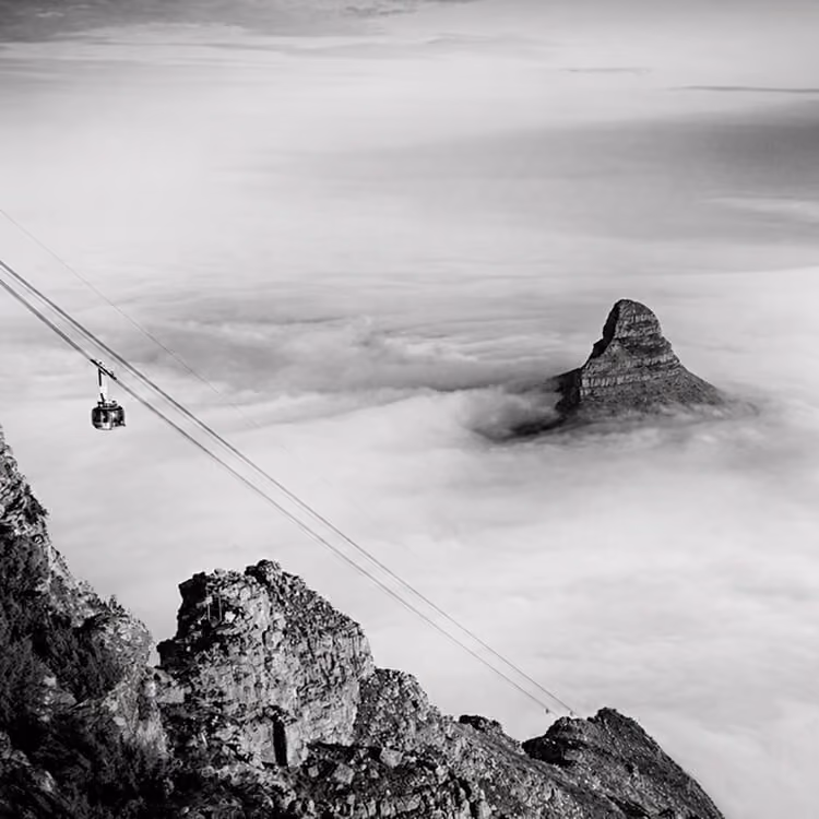 Cable car ascending Table Mountain above clouds with dramatic mountain peak in Cape Town.