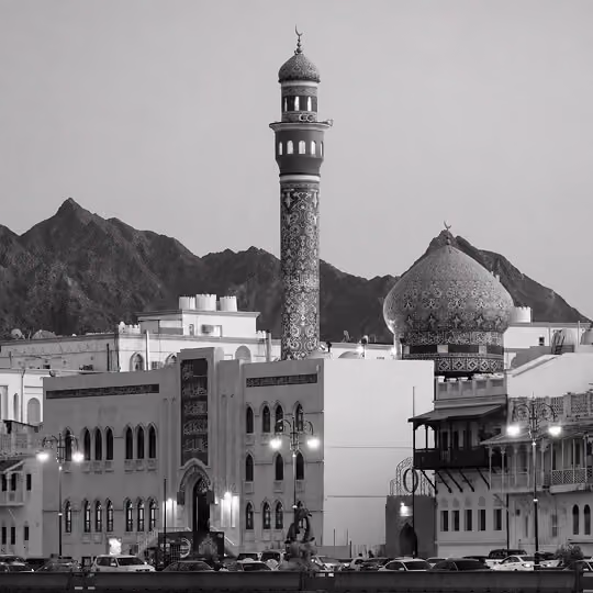 Ornate mosque with patterned minaret and dome set against mountainous landscape in Oman.