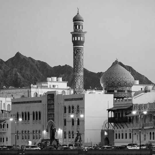 Ornate mosque with patterned minaret and dome set against mountainous landscape in Oman.