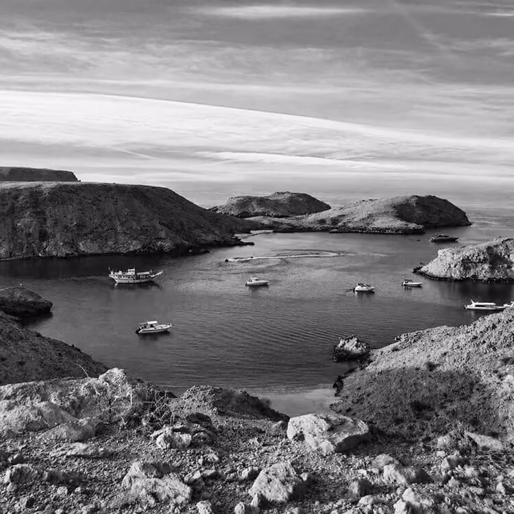 Rocky coastal bay in Muscat with boats anchored in calm water surrounded by cliffs.