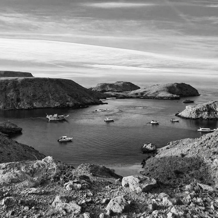 Rocky coastal bay in Muscat with boats anchored in calm water surrounded by cliffs.