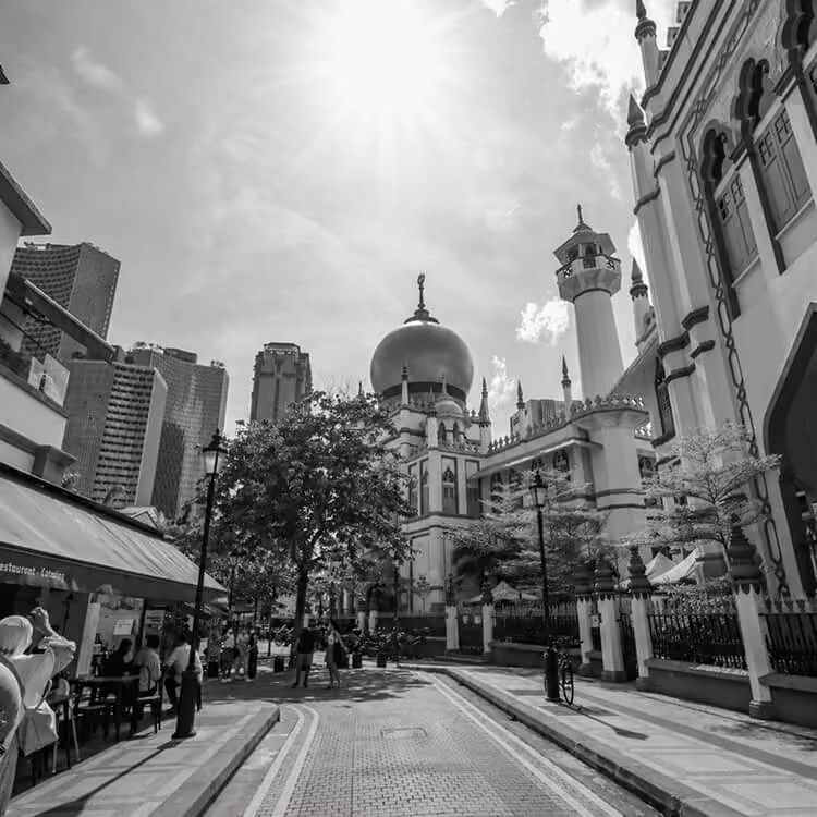 Street view of Sultan Qaboos Grand Mosque area with pedestrians and surrounding city buildings.