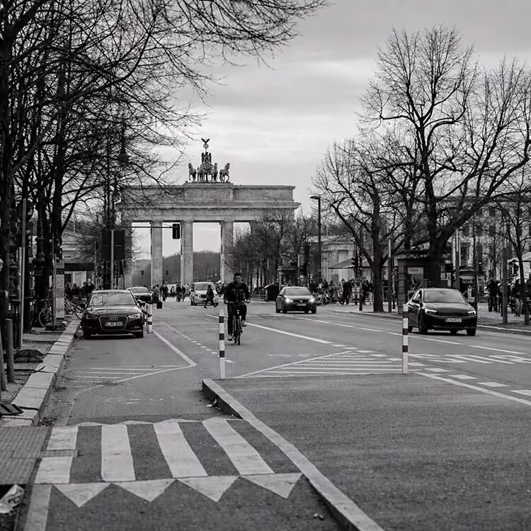 Brandenburg Gate in Berlin with cyclists and traffic along a busy city street.