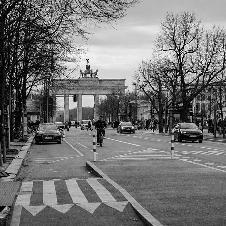 Brandenburg Gate in Berlin with cyclists and traffic along a busy city street.