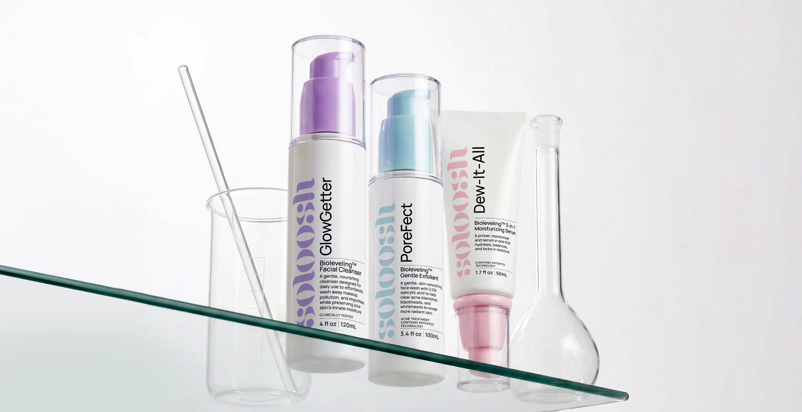 Soloosh skincare products displayed on a glass shelf with lab-style beakers, featuring GlowGetter cleanser, Porefect exfoliant, and Dew-It-All serum.