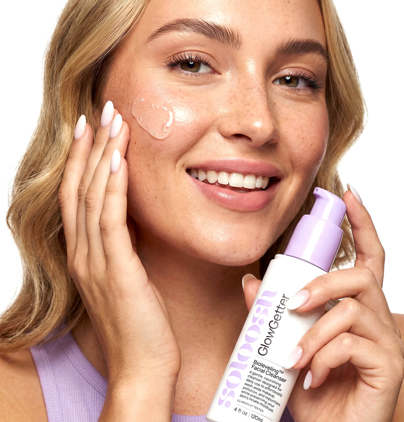 Woman applying serum to her face while holding Soloosh GlowGetter facial cleanser bottle.