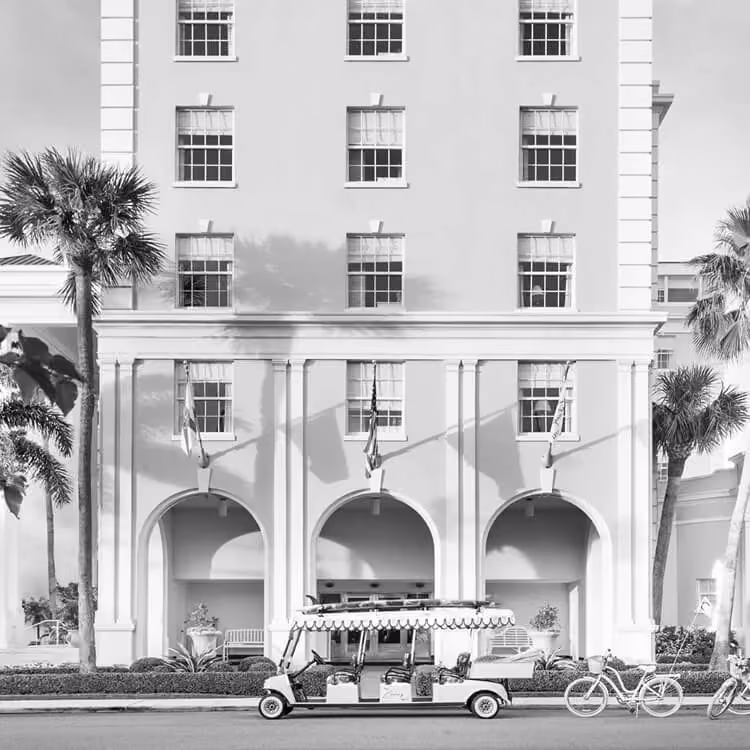 Elegant resort hotel entrance with bicycles, palm trees, and a vintage-style shuttle cart.