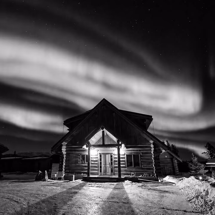 Remote Yukon log cabin illuminated beneath the northern lights on a winter night.