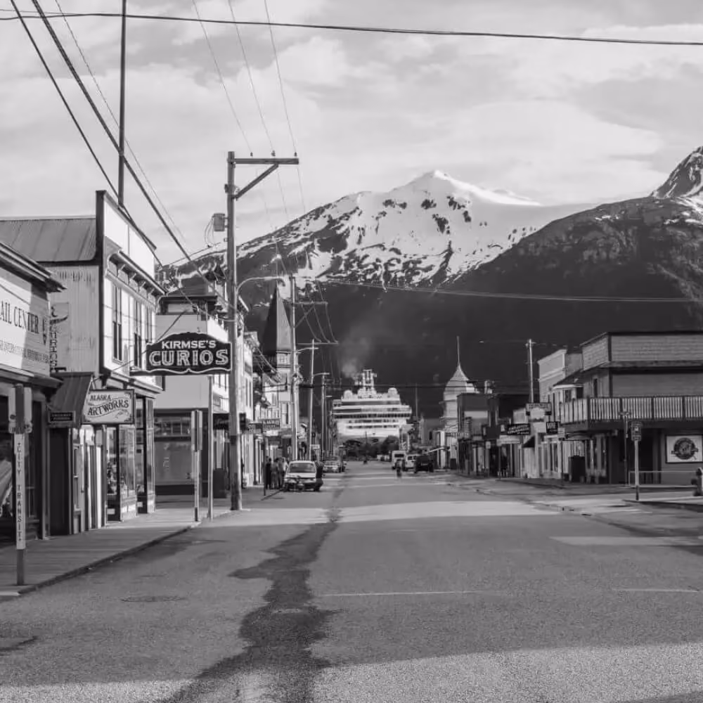Historic Yukon town street leading toward snow-covered mountains and a docked cruise ship.Historic Yukon town street leading toward snow-covered mountains and a docked cruise ship.