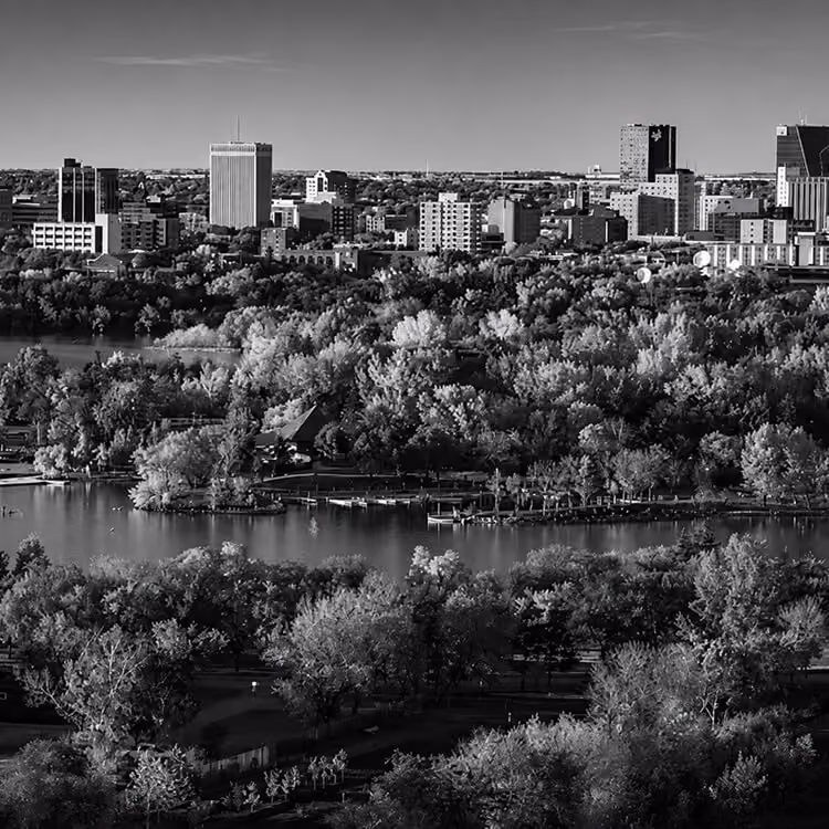 Aerial view of Regina’s urban skyline surrounded by trees and waterfront landscapes.
