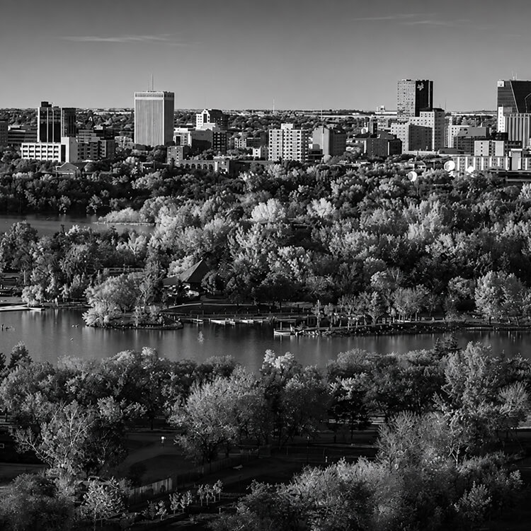 Aerial view of Regina’s urban skyline surrounded by trees and waterfront landscapes.