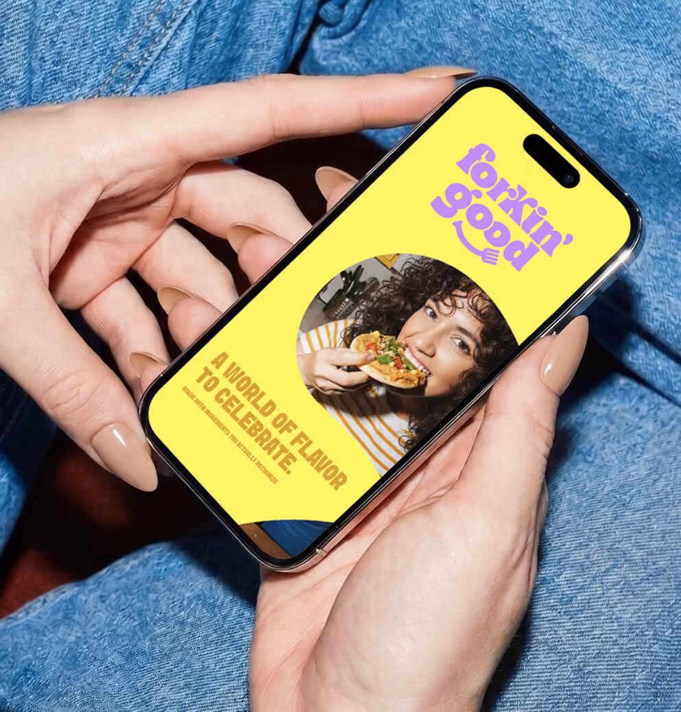 Person holding a smartphone displaying the Forkin’ Good mobile website featuring bright yellow branding, food photography, and playful typography.