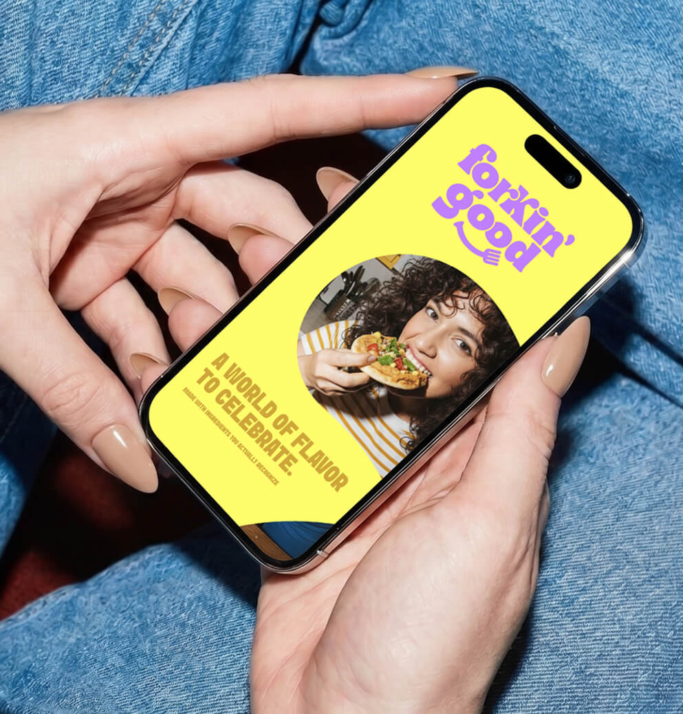 Person holding a smartphone displaying the Forkin’ Good mobile website featuring bright yellow branding, food photography, and playful typography.